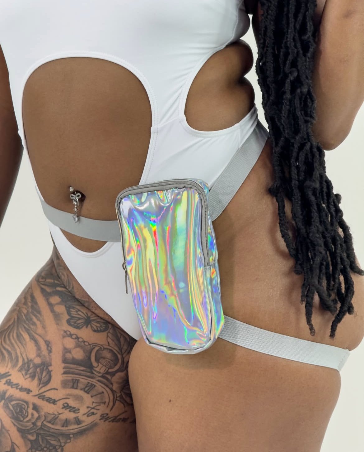 Person wearing a white outfit with cut-out design and holographic thigh bag on a plain background
